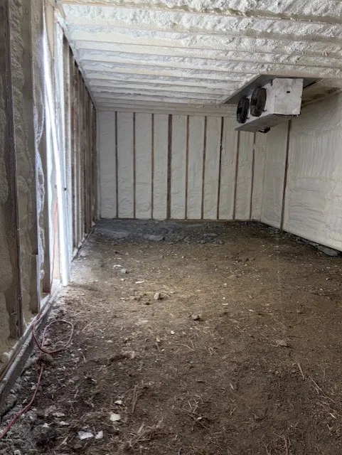 Ceiling and one wall covered in closed-cell spray foam while adjacent walls remain unsprayed